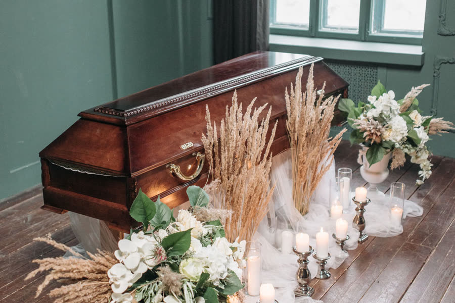 Opgebaarde kist met droogbloemen en kaarsen in een aula
